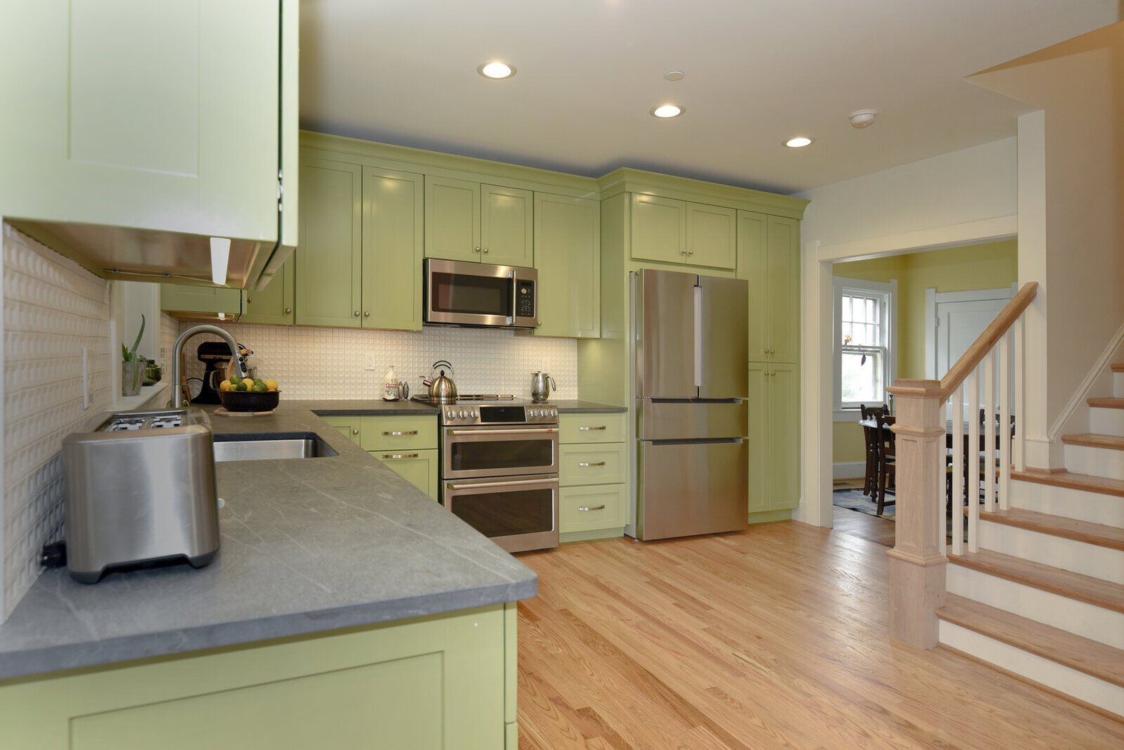 Modern kitchen with green cabinets and stainless steel appliances in a remodeled historic home by Villa Builders in Annapolis, MD