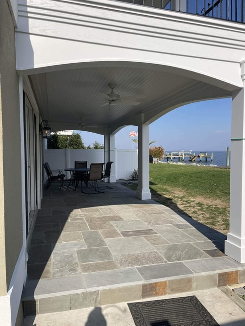 Modern outdoor living area with a covered patio and natural stone flooring by Villa Builders in Annapolis, MD