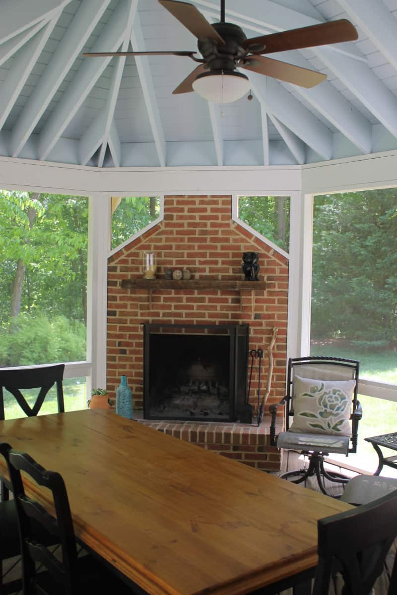 Interior of a screened porch with brick fireplace and ceiling fan in central Maryland by Villa Builders